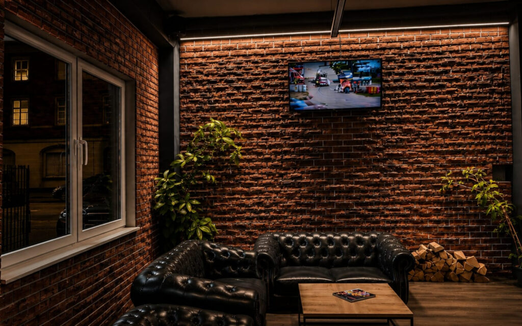 Lounge Limitless Recklinghausen Lounge Bereich mit Chesterfield Sofas, Backsteinwand und TV im Limitless Recklinghausen