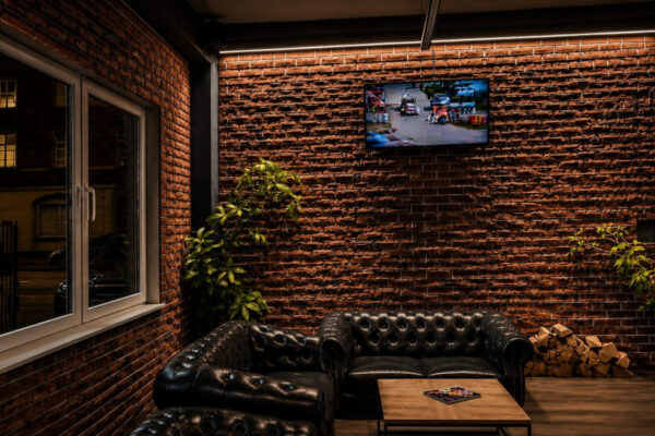 Lounge Limitless Recklinghausen Lounge Bereich mit Chesterfield Sofas, Backsteinwand und TV im Limitless Recklinghausen